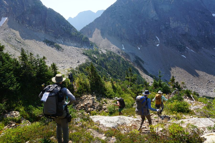 Backpackers descending off-trail into a mountain cirque