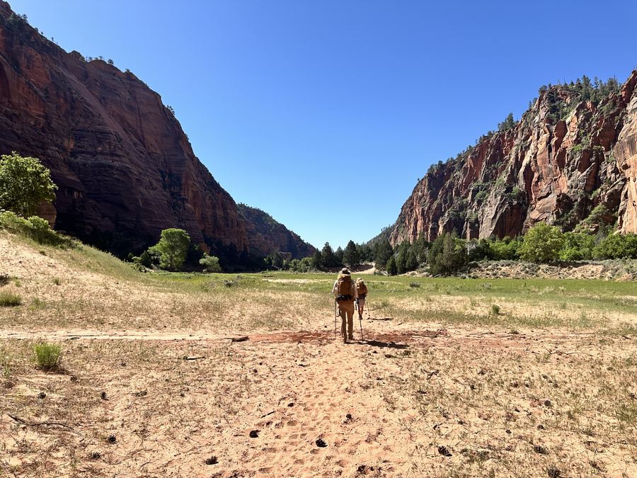 Backpackers walking a sandy canyon floor between sandstone cliffs