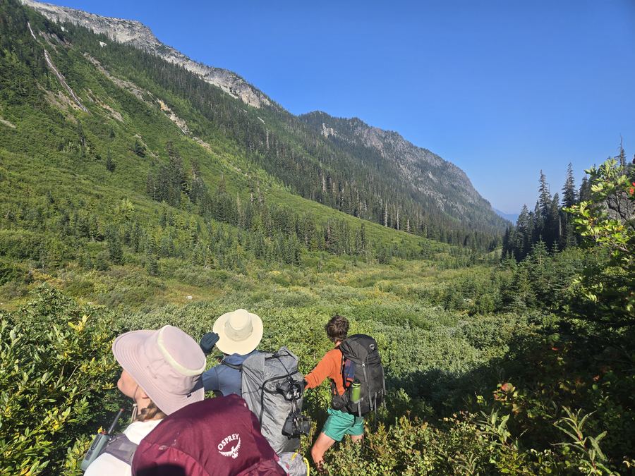 Crew route-finding through brush below towering valley walls